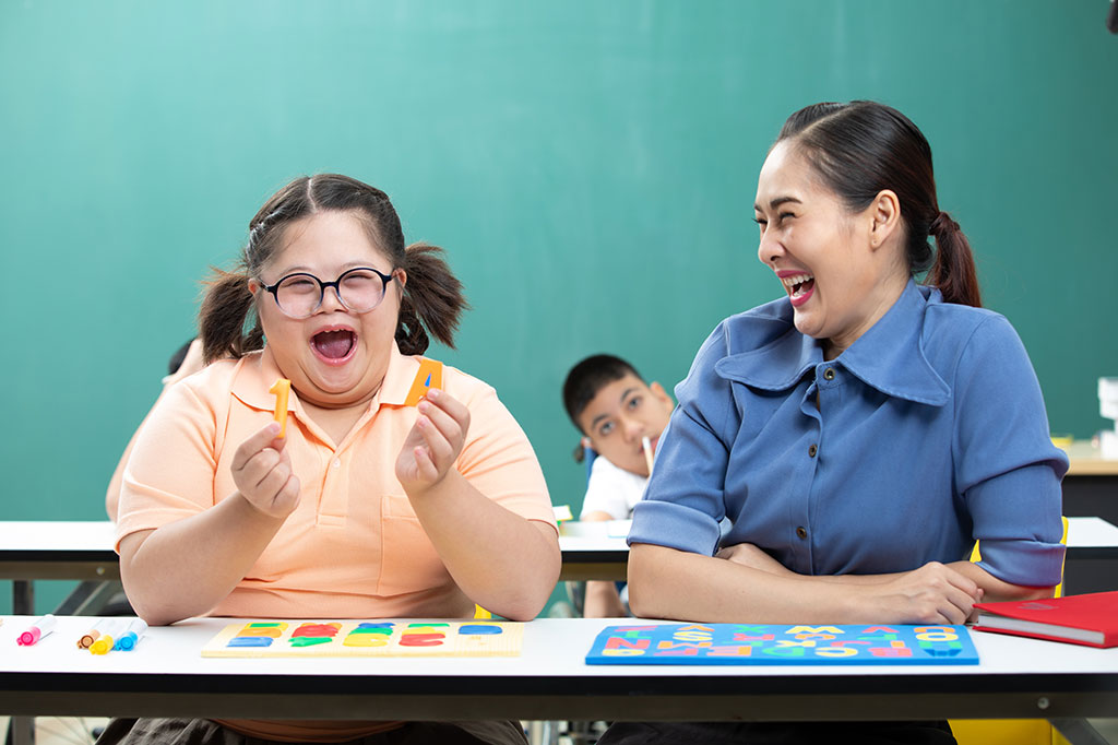 Child with Down's Syndrome laughing with teacher.